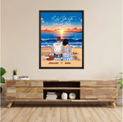 Personalized couple framed canvas of two people sitting together on a beach picnic blanket at sunset, with a custom romantic quote above the ocean and their names written in the sand — LOVECOUPLET